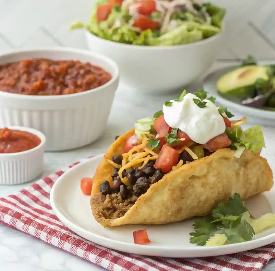 Homemade Taco Bell Chalupa Supreme served on a plate with seasoned beef, black beans, shredded cheese, diced tomatoes, lettuce, and a dollop of sour cream.